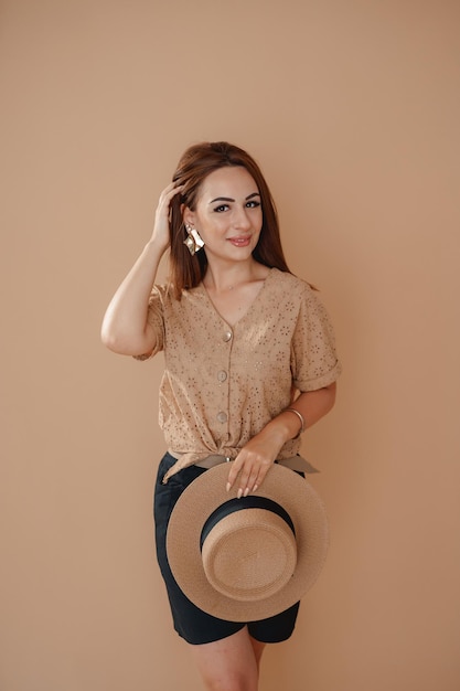 a girl in a beige shirt on a beige background holding a hat in her hands