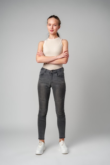 Girl in beige tank top and grey jeans on gray background