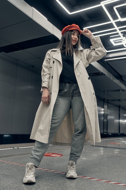 Girl in a beige trench coat in the subway waiting for the train on the platform