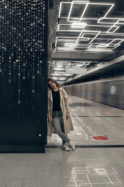 Girl in a beige trench coat in the subway waiting for the train on the platform