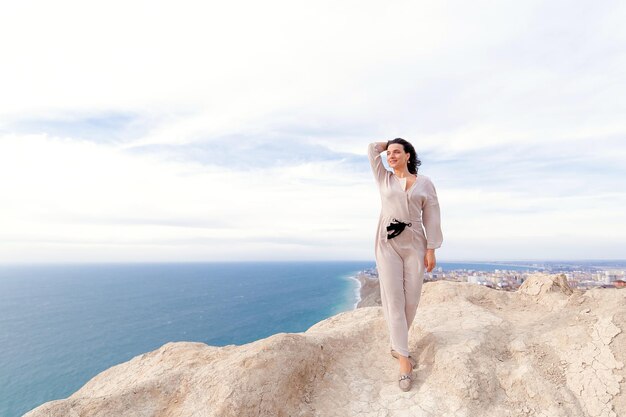 a girl in beige walks on a rock against the background of the sea