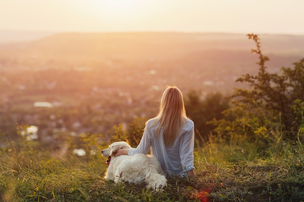 girl and big dog sitting on the mountain at sunset