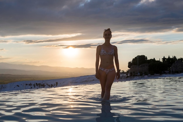 Girl in a bikini enjoying a hot spring pool with calciumcoated cliffs in Pamukkale on sunset