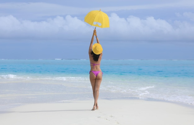 девушка в бикини с желтым зонтиком на морском песке