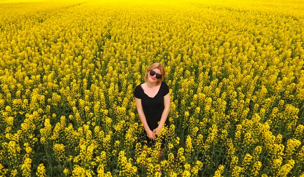 Photo a girl in a black dress among the colors of rape in the field w