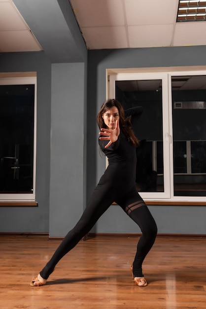 Девушка в черном платье тренируется в танцевальной студии