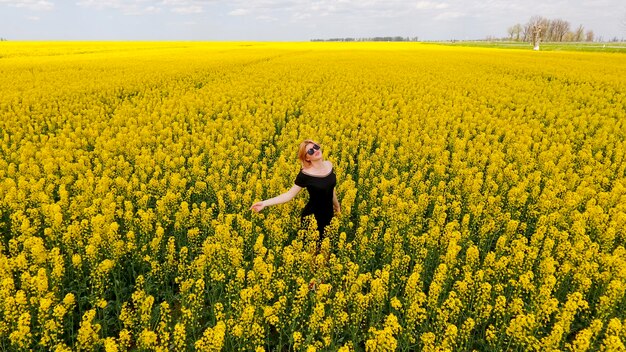 A girl in a black dress among the colors of rape in the field W