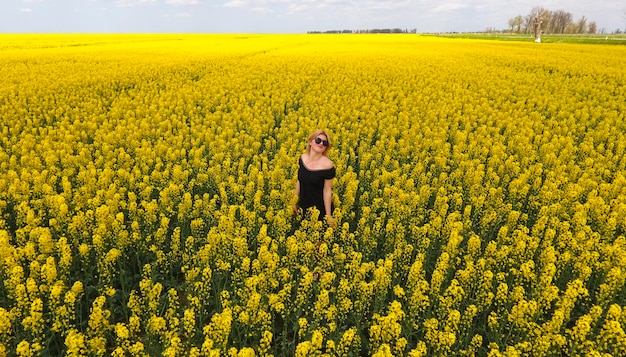 A girl in a black dress among the colors of rape in the field W