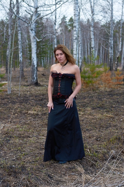 A girl in a black dress in the forest.the girl is a witch in a black corset.