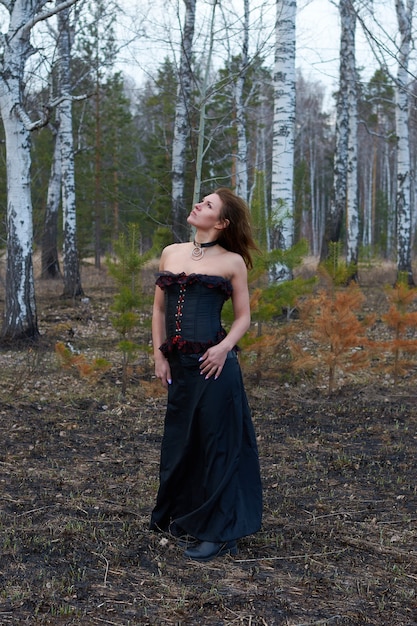 森の中の黒いドレスを着た女の子。女の子は黒いコルセットの魔女です。