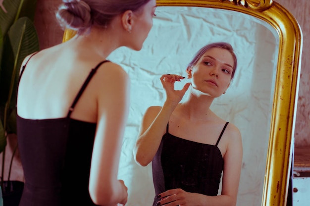 A girl in a black dress looks at the reflection in the mirror