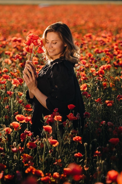 A girl in a black dress on a poppy field at sunset