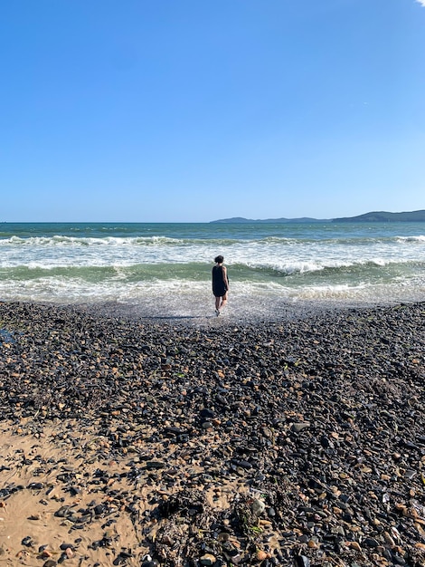 A girl in a black dress walks along the seashore