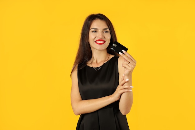 Girl in black dress with credit card on yellow background.