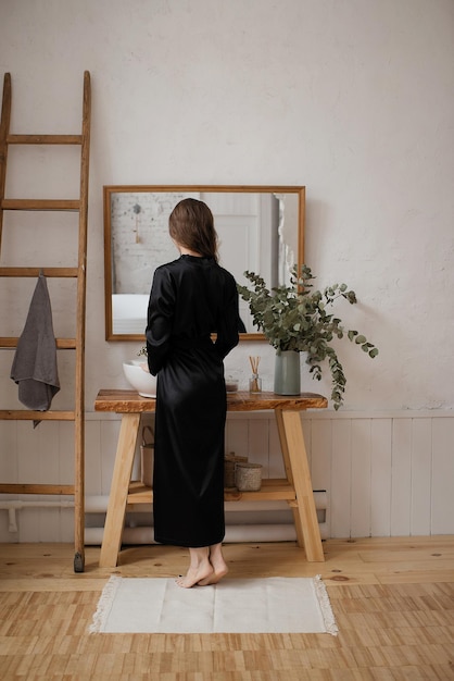 A girl in a black robe stands at the mirror in the bathroom