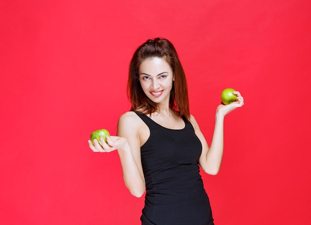 Girl in black singlet holding green apples.