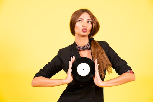 Girl in a black suit on a yellow background with a record in her hands, music, the girl shows emotions