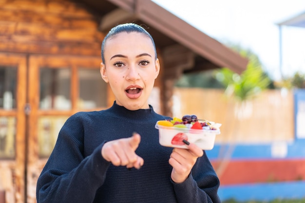 A girl in a black sweater holds a bowl of fruit.