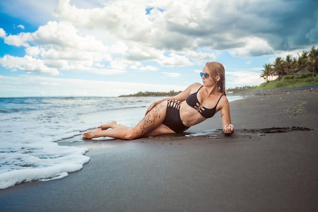 Girl in the black swimsuit and sunglasses lies on the beach