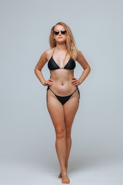 Girl in a black swimsuit and sunglasses on a light gray background