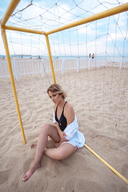 a girl in a black swimsuit and a white shirt is sitting at the gate for beach soccer