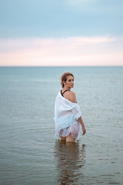 a girl in a black swimsuit and a white shirt is standing in the sea