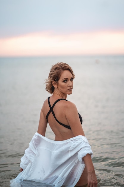 a girl in a black swimsuit and a white shirt is standing in the sea