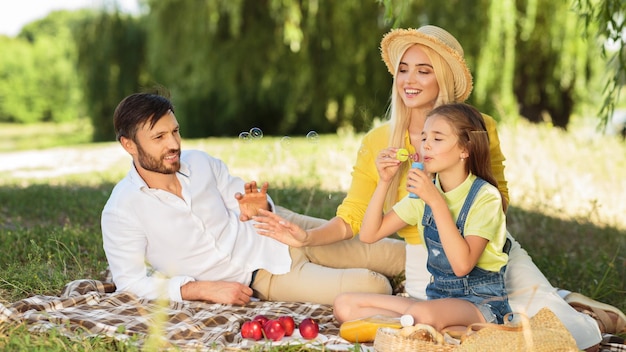 Girl blowing bubbles enjoying day with parents in park