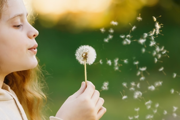 Ragazza che soffia dente di leone nel parco primaverile concetto sano medico