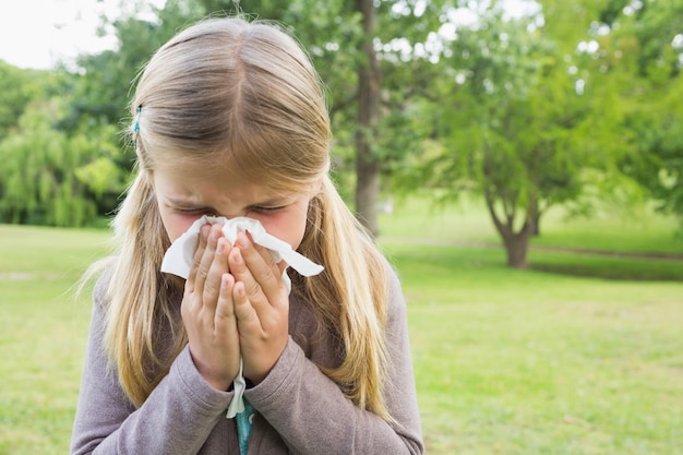 Girl blowing nose with tissue paper at park