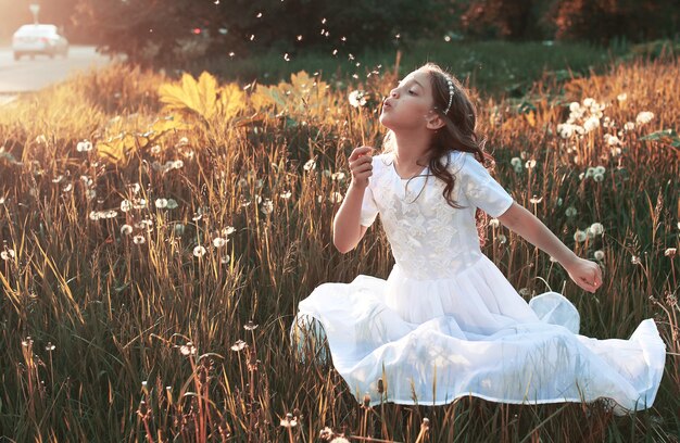 Girl blowing seeds from a flower dandelion in the autumn afternoon