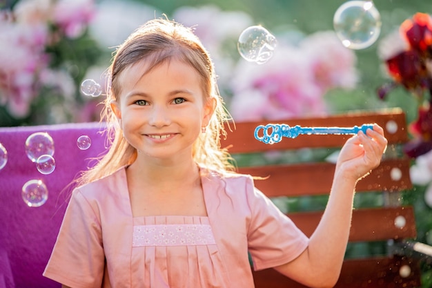 Girl blows soap bubbles against flowers in the garden. On the face of emotions of surprise and admiration.