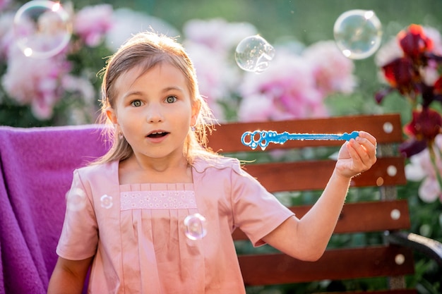 La ragazza soffia bolle di sapone contro i fiori nel giardino. di fronte a emozioni di sorpresa e ammirazione.