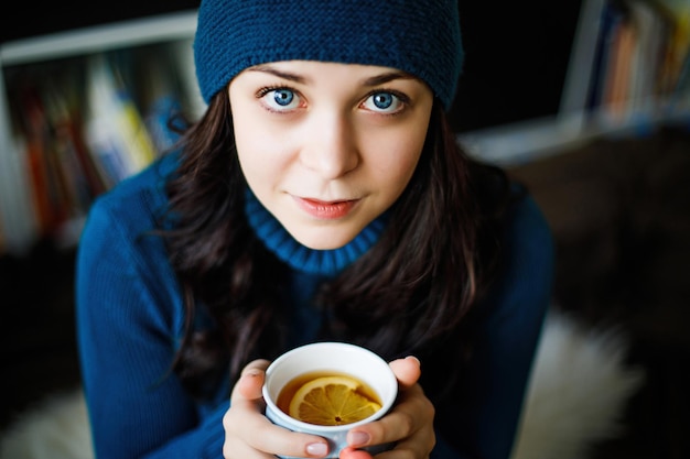 A girl in blue clothes drinks tangerine tea from a blue mug