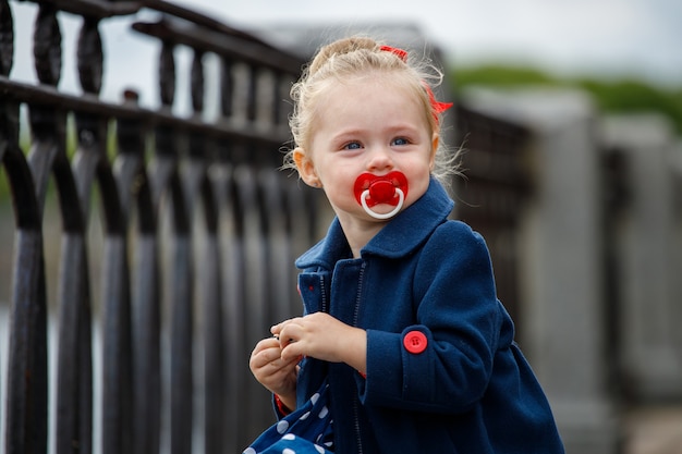 Girl in a blue coat with a pacifier in her mouth on the street