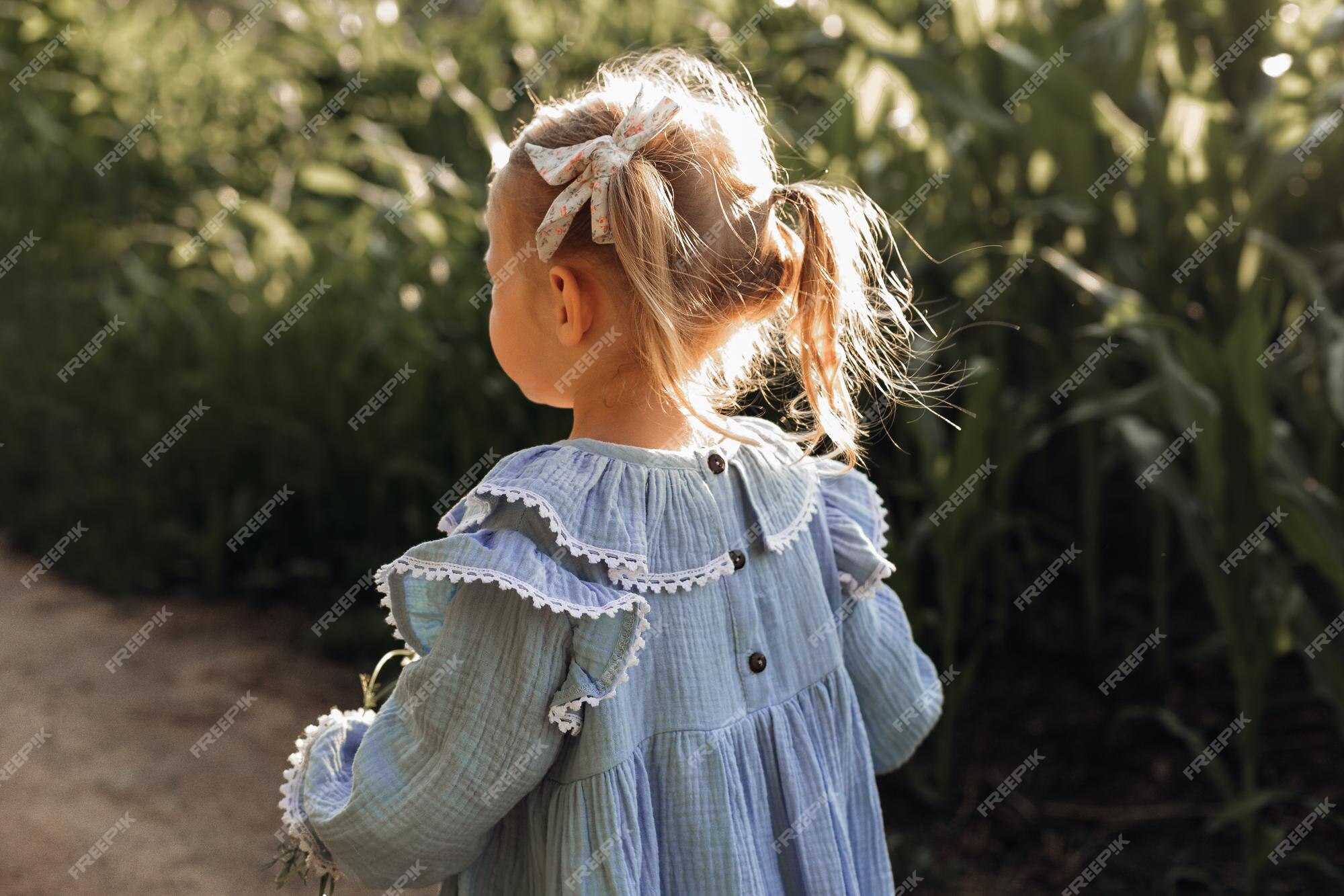 Premium Photo | Girl in blue cotton dress 3 years old walks on field.  children's clothing made of natural materials. happy childhood.  agricultural industry. unity with nature. hairstyle for children with bows.