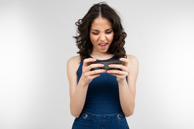 Girl in a blue dress holds a smartphone in horizontal position on a gray studio with copy space