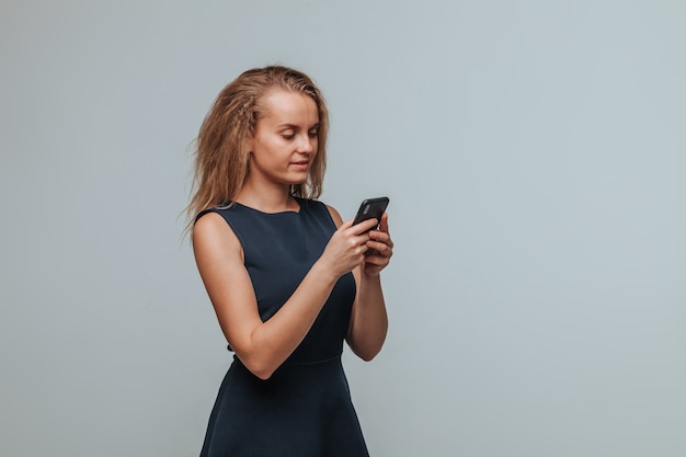 A girl in a blue dress is typing a message in the phone on a gray background