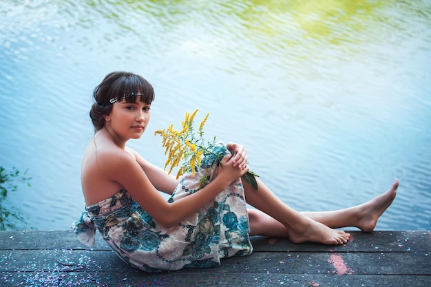 Girl in blue dress sitting by a lake