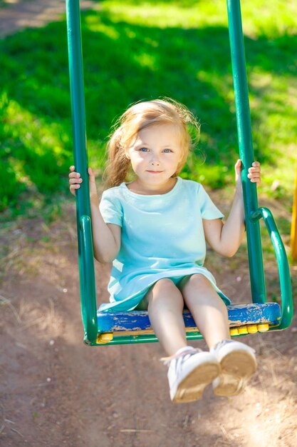 Girl in a blue dress swinging on a swing in nature