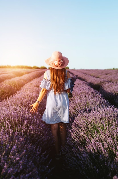 A girl in blue dress walking trough lavender fields at sunset.