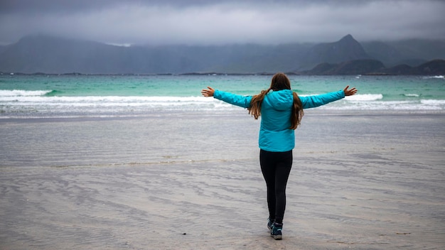 a girl in a blue jacket admires the gloomy landscape on a beach in the lofoten islands in norway