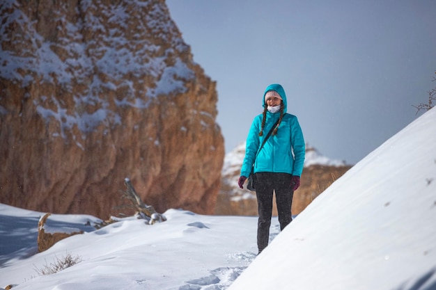 Girl in blue jacket hiking in snowy bryce canyon national park\
in winter, snowy red rocks in utah