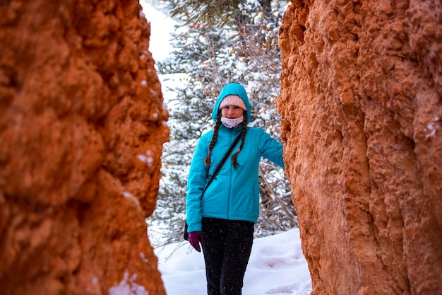 girl in blue jacket hiking through snowdrifts among massive rocks of bryce canyon in freezing winter