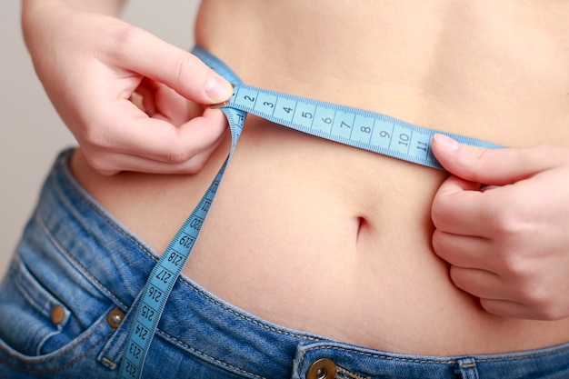 Girl in blue jeans is measuring her waist