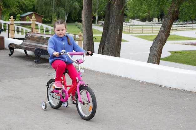 A girl in a blue sweater and pink pants rides a pink Bicycle bike along the river Bank.