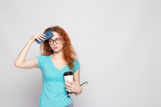 A girl in a blue tshirt with a phone and coffee on a light background