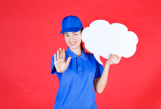 Foto ragazza in uniforme blu e berretto che tiene una lavagna a forma di nuvola e ferma qualcosa con il gesto della mano.