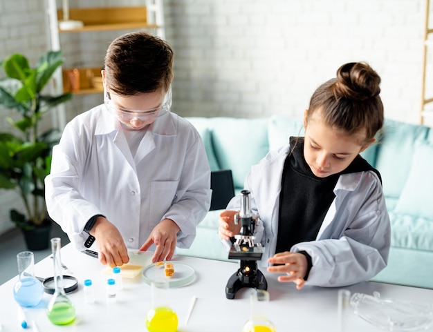 한 소녀와 소년이 학교 튜브와 현미경의 실험실에서 실험을 하고 있다