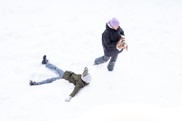 Ragazza e ragazzo si divertono all'aria aperta, il giorno nevica, sorella e fratello che ridono stelle filanti cane giocano a neve in abiti caldi invernali